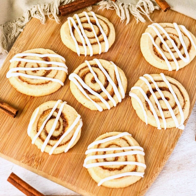 Seven cinnamon swirl cookies with white icing on a wooden board.