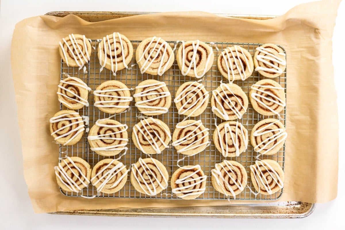 Round cookies with white icing drizzle on a cooling rack and parchment paper.