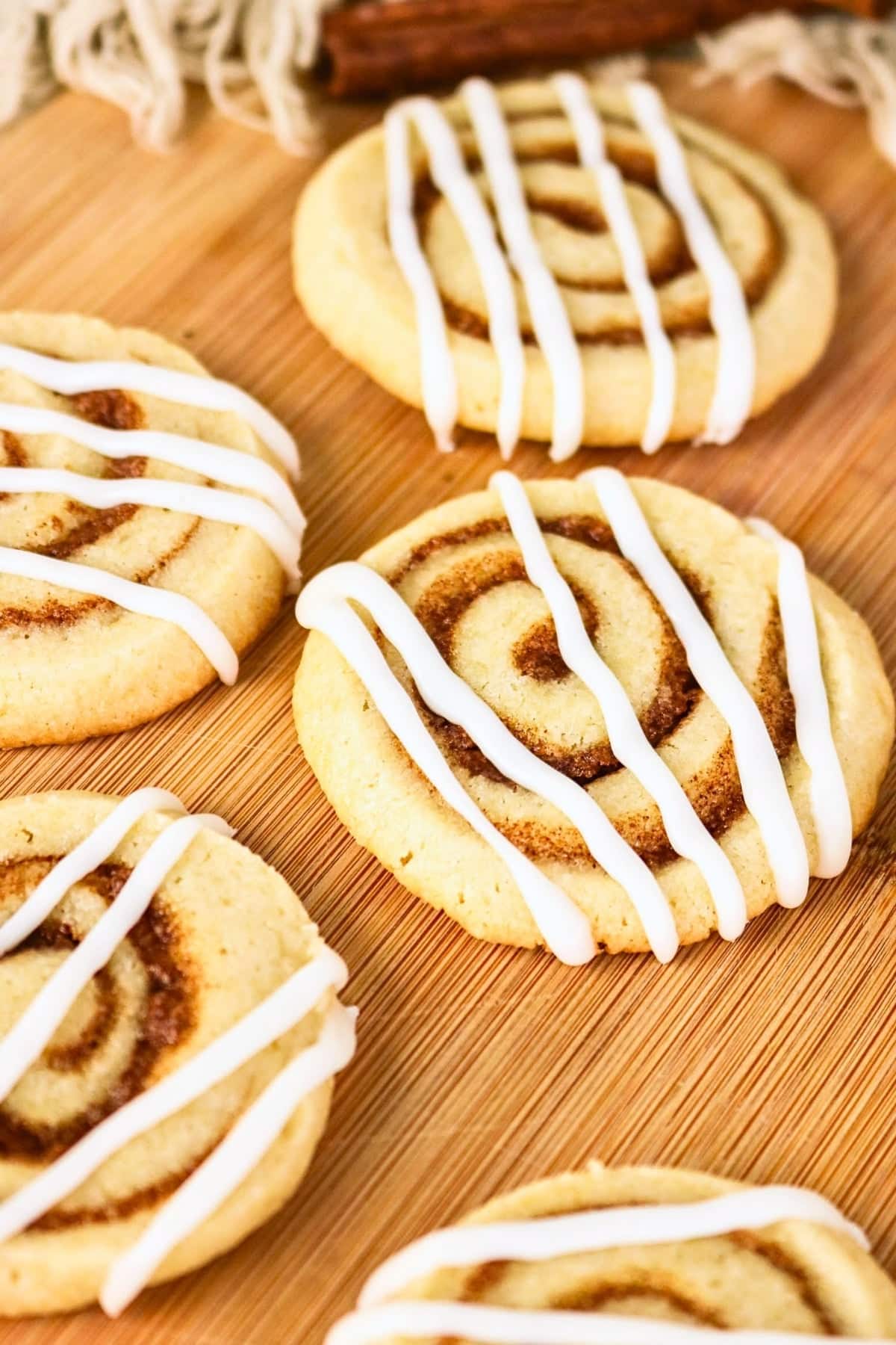 Cinnamon swirl cookies with white icing on a wooden surface.