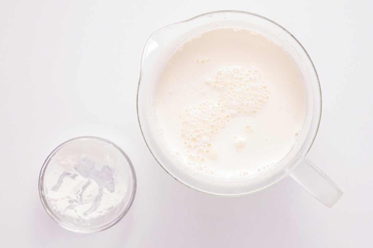 Pitcher of milk next to a small glass of white powder on a white background.