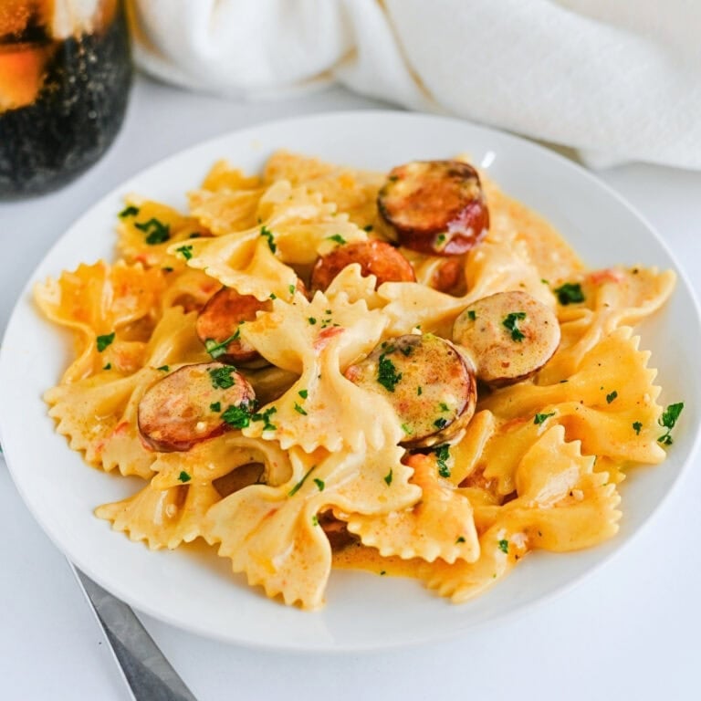 Bowtie pasta with sliced sausage and creamy sauce, garnished with herbs.