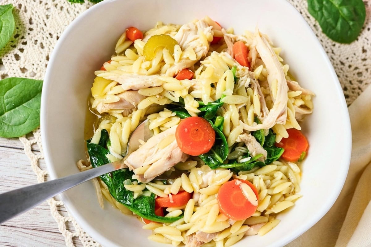 Bowl of orzo pasta with chicken, carrots, celery, and spinach.