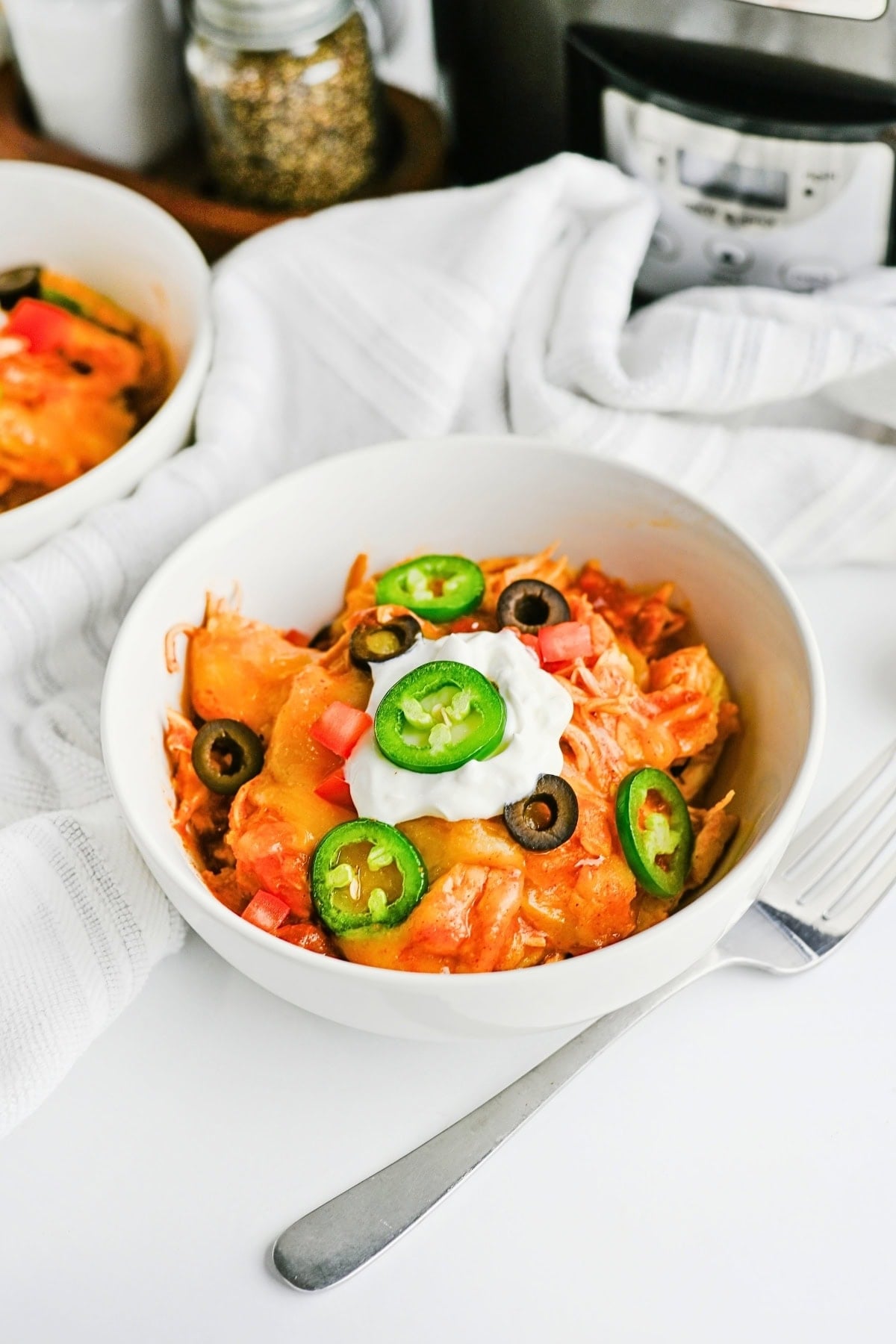 Bowl of cheesy chicken topped with jalapeños, olives, tomatoes, and sour cream.