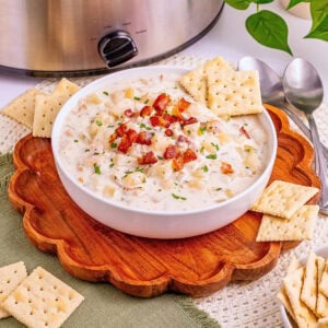 Creamy soup with bacon in a bowl, surrounded by crackers and spoons.