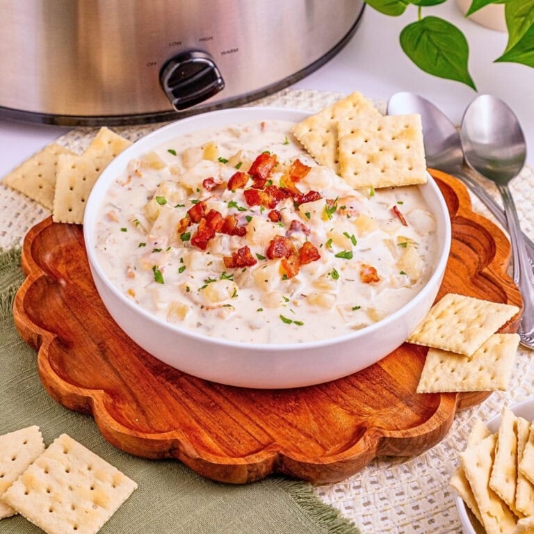 Creamy soup with bacon in a bowl, surrounded by crackers and spoons.