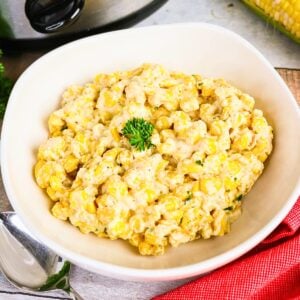 Creamed corn in a white bowl, topped with a sprig of parsley.