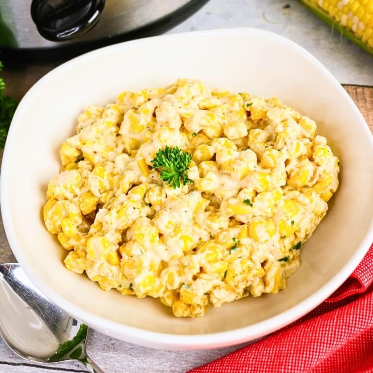 Creamed corn in a white bowl, topped with a sprig of parsley.