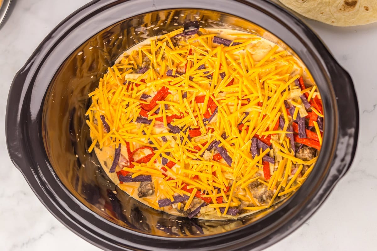 Shredded cheese and tortilla strips in a slow cooker, ready to be cooked.
