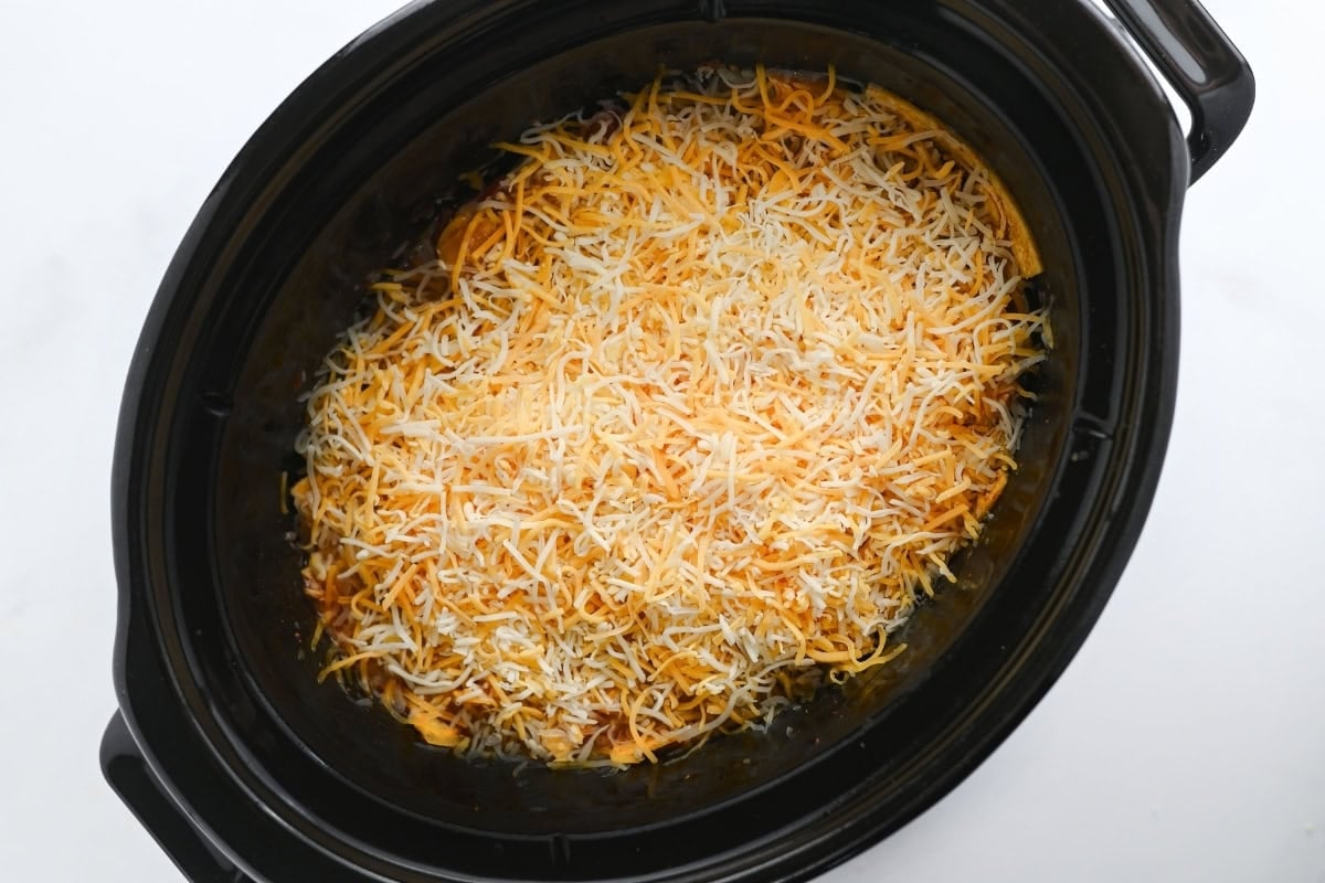 Crockpot filled with shredded cheese on top of food, ready to be cooked.