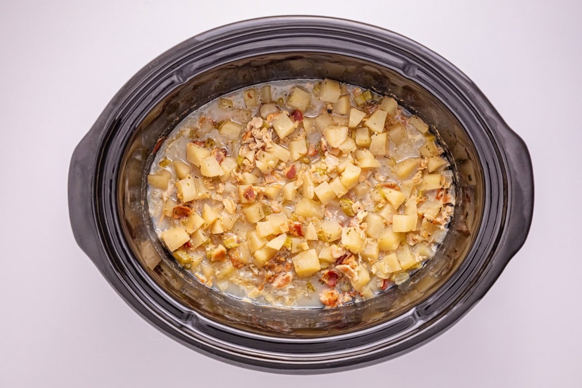 Diced potatoes and bacon cooking in a black slow cooker.