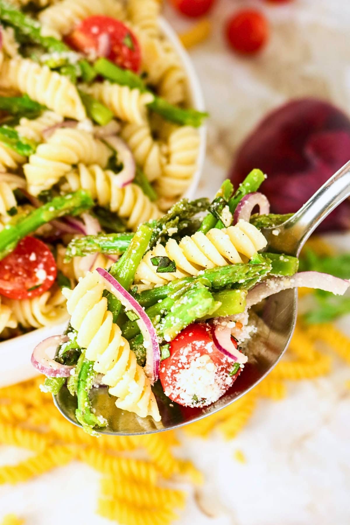 A spoonful of pasta salad with tomatoes, asparagus, and red onions.