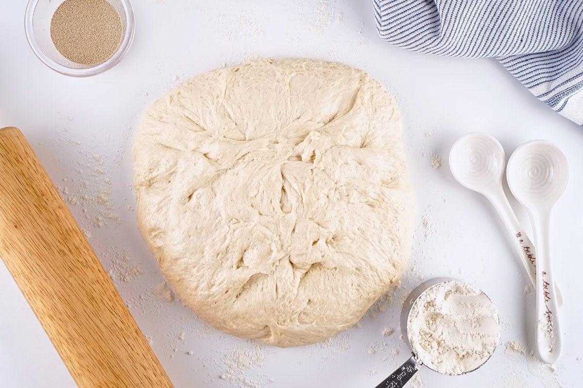 Bread dough on a floured surface with baking tools and flour nearby.