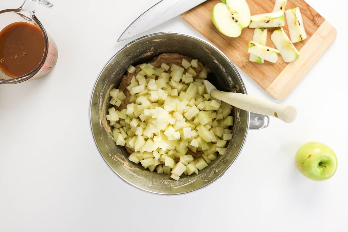 Chopped apples in a mixing bowl with a spoon, knife, and apple pieces nearby.