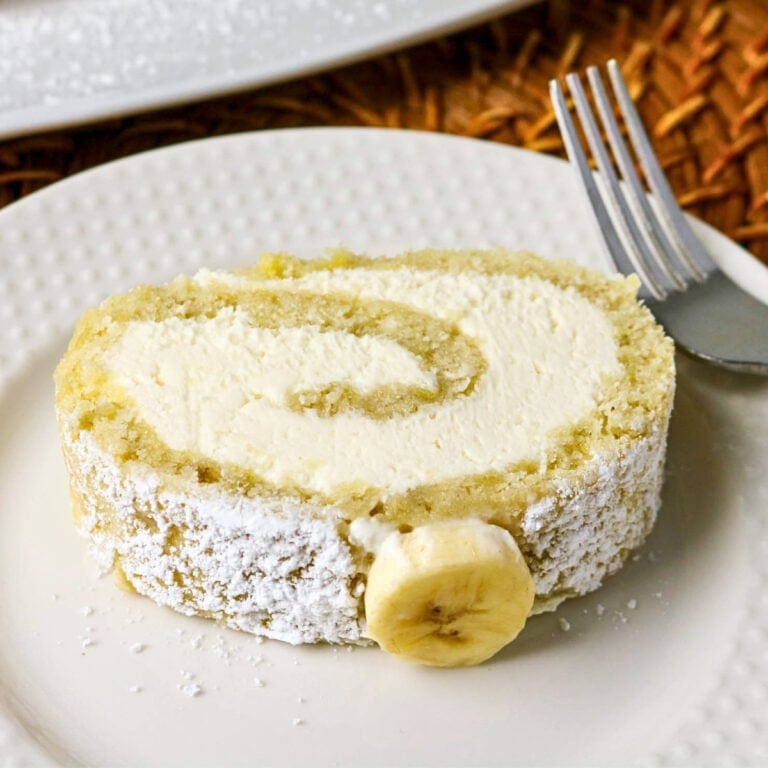 Rolled sponge cake with cream filling and a banana slice on a white plate.
