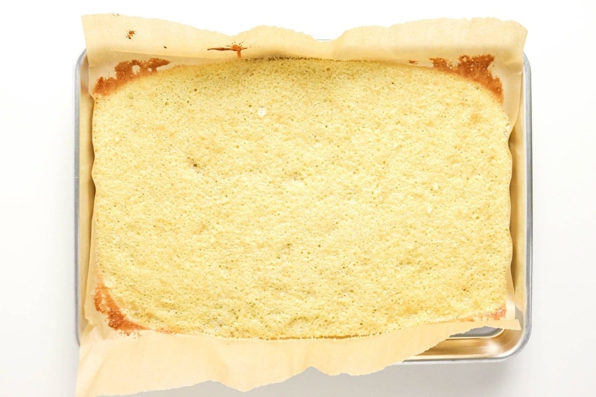 Rectangular baked cake layer on parchment paper in a metal baking pan.