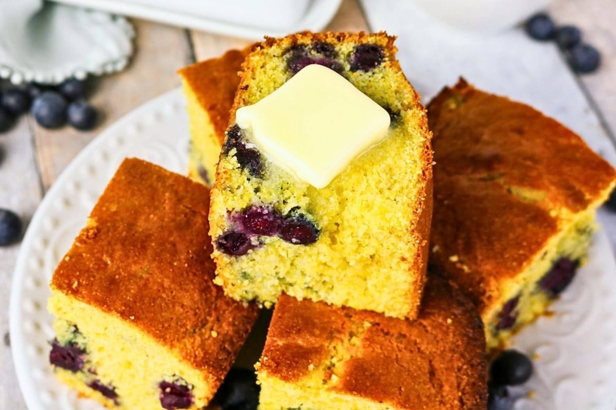 Slices of blueberry cornbread with a pat of butter on top, on a white plate.