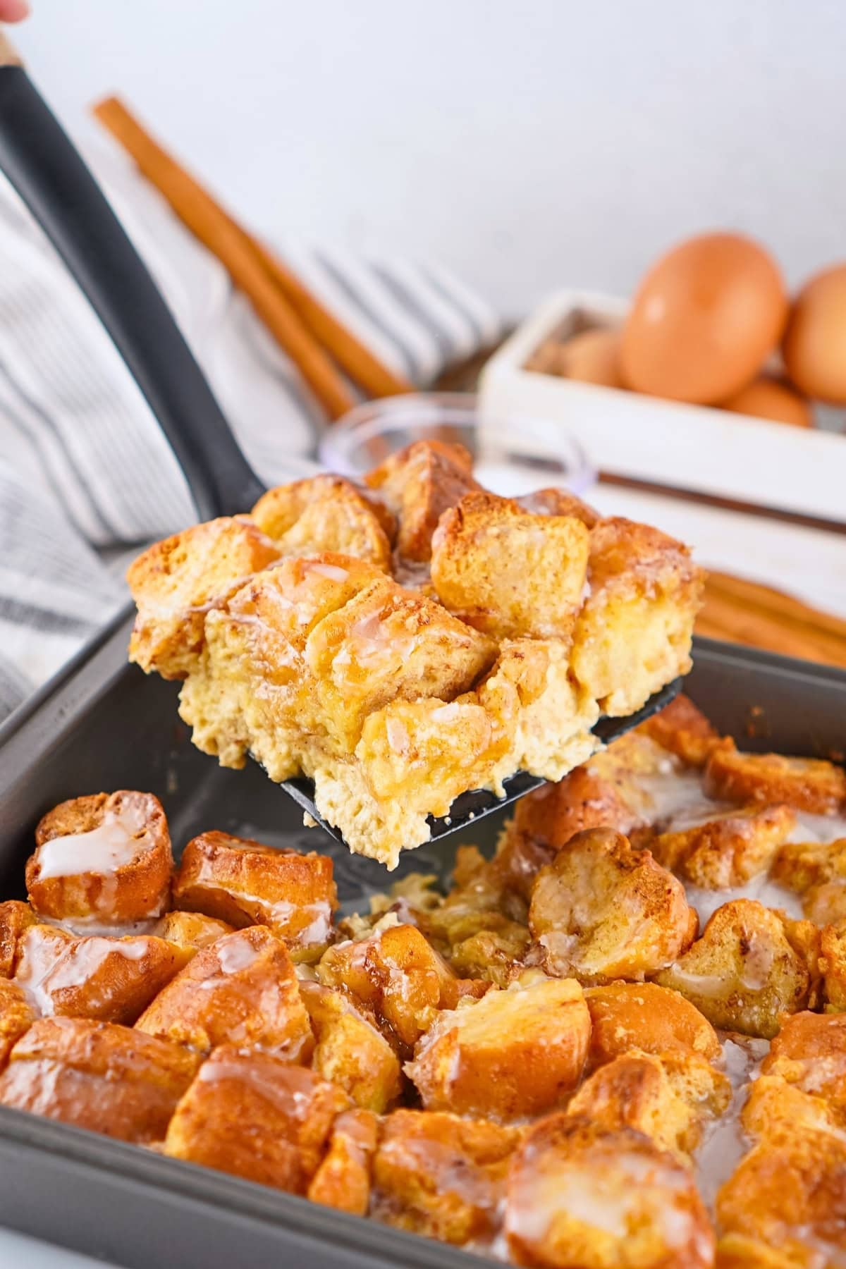 A spatula lifts a piece of sweet, baked French toast casserole from a pan.