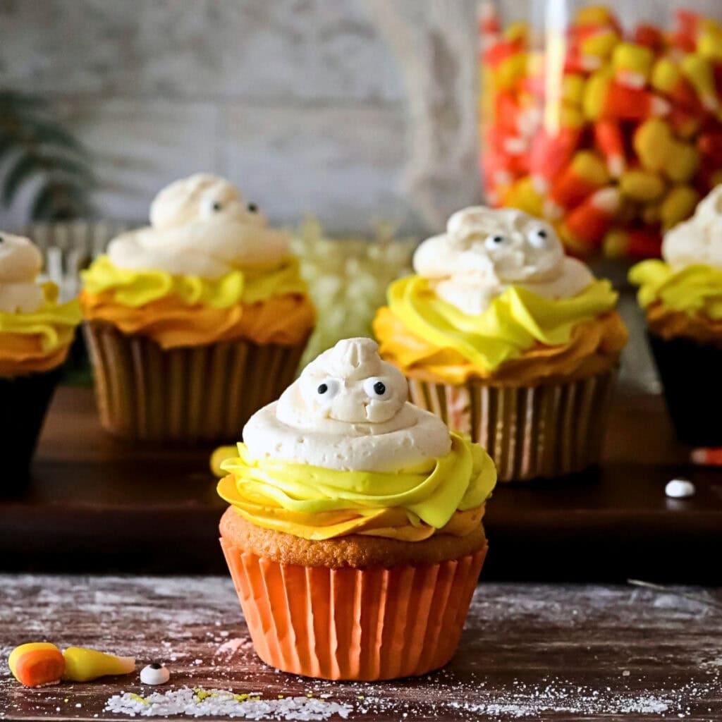 Cupcakes with yellow frosting and candy eyes, with candy corn in the background.
