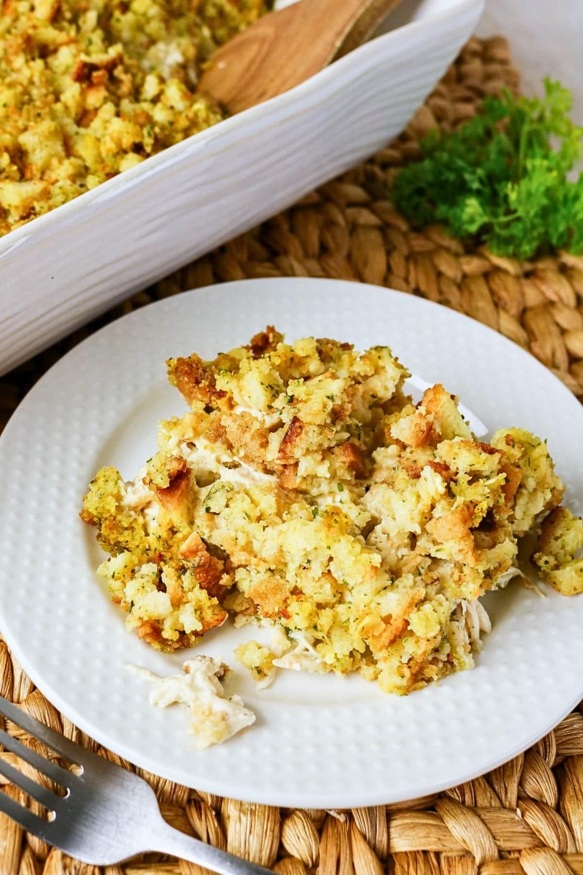 A serving of stuffing casserole on a white plate beside a baking dish.