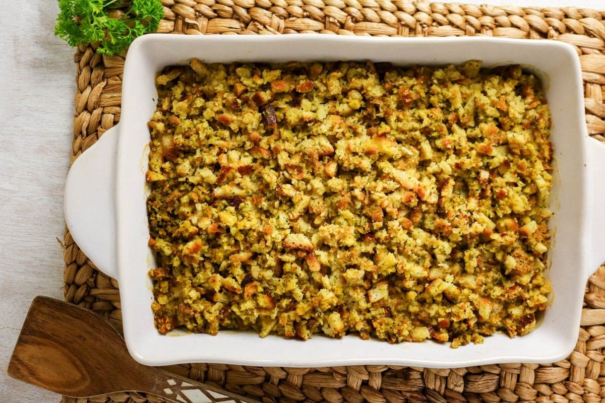 Golden baked stuffing in a white casserole dish on a woven placemat.