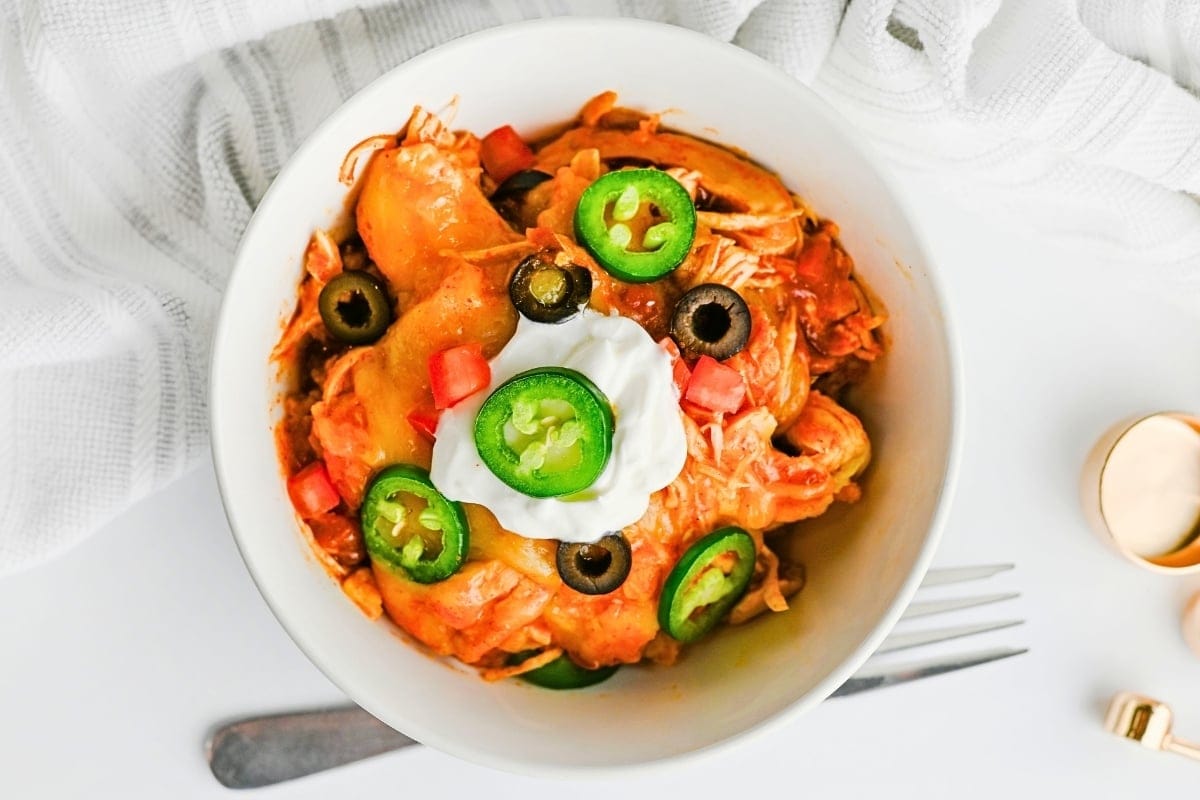 Bowl of cheesy chicken topped with jalapeños, olives, tomato, and sour cream.