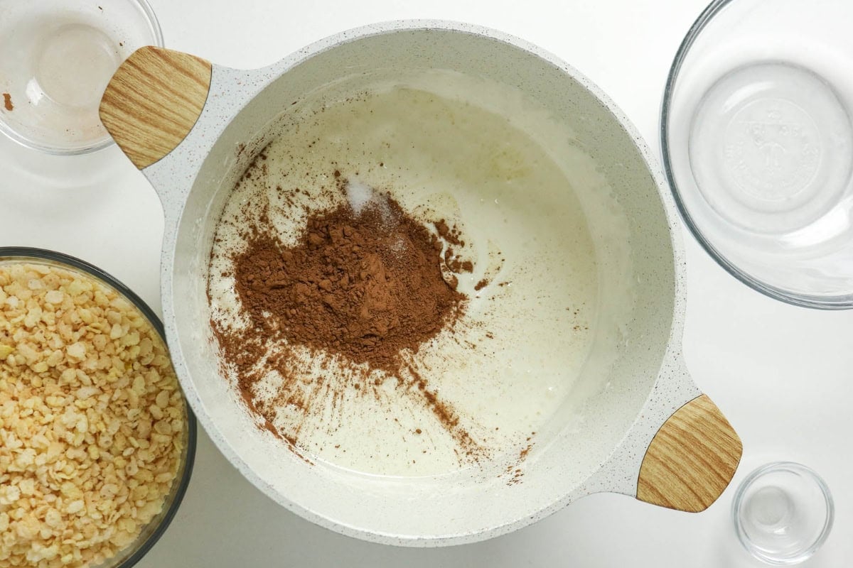 Bowl with milk, cocoa powder, and cereal, surrounded by empty glass bowls.