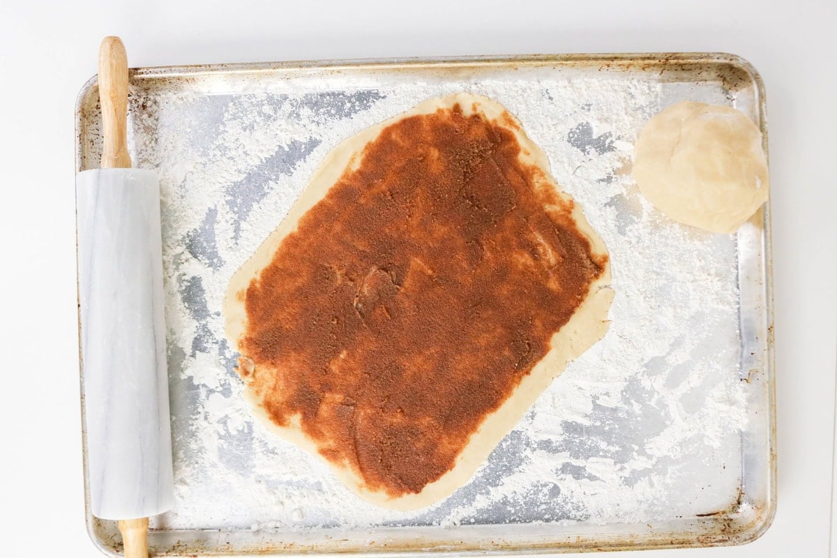 Dough rolled with cinnamon filling, rolling pin, and dough ball on floured pan.
