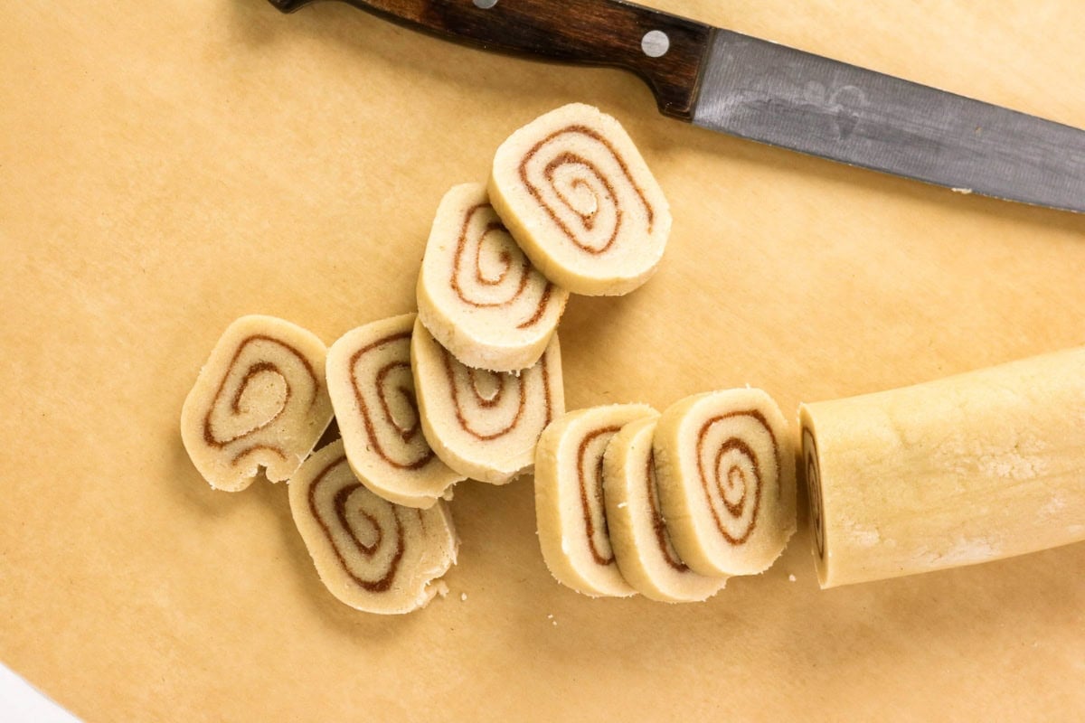Sliced cinnamon roll dough with knife on a light surface.
