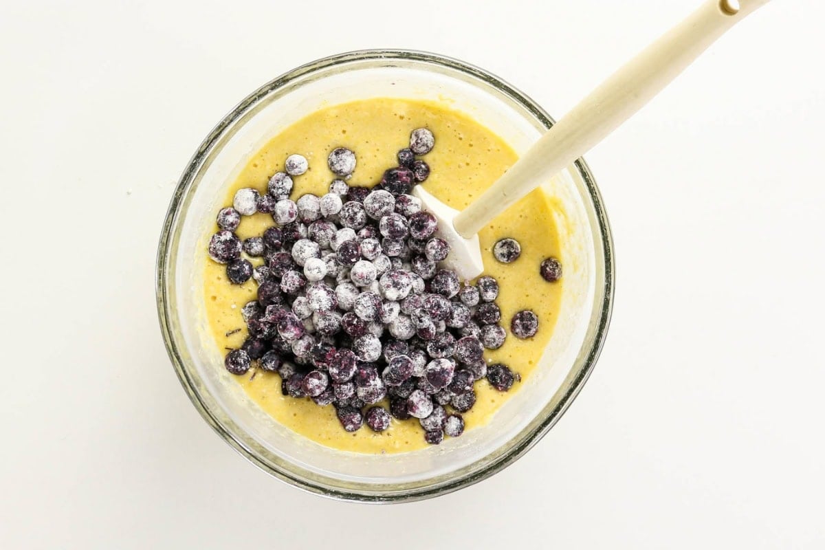 Blueberries in batter in a glass bowl with a spoon, seen from above.