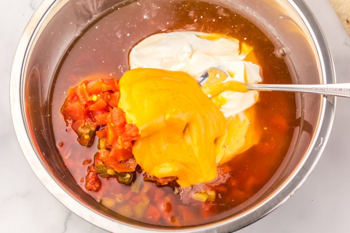 Bowl with sour cream, nacho cheese, salsa, and sauce being mixed with a spoon.