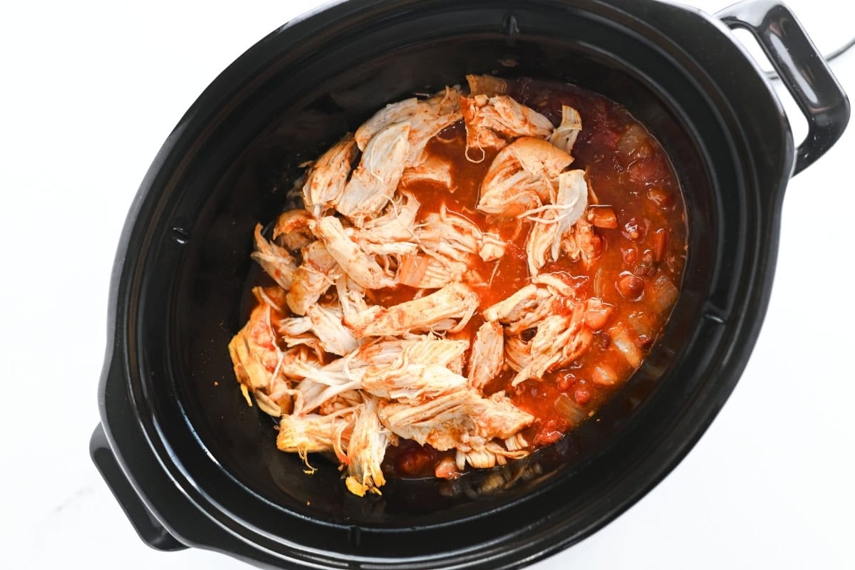 Shredded chicken in tomato sauce inside a black slow cooker.
