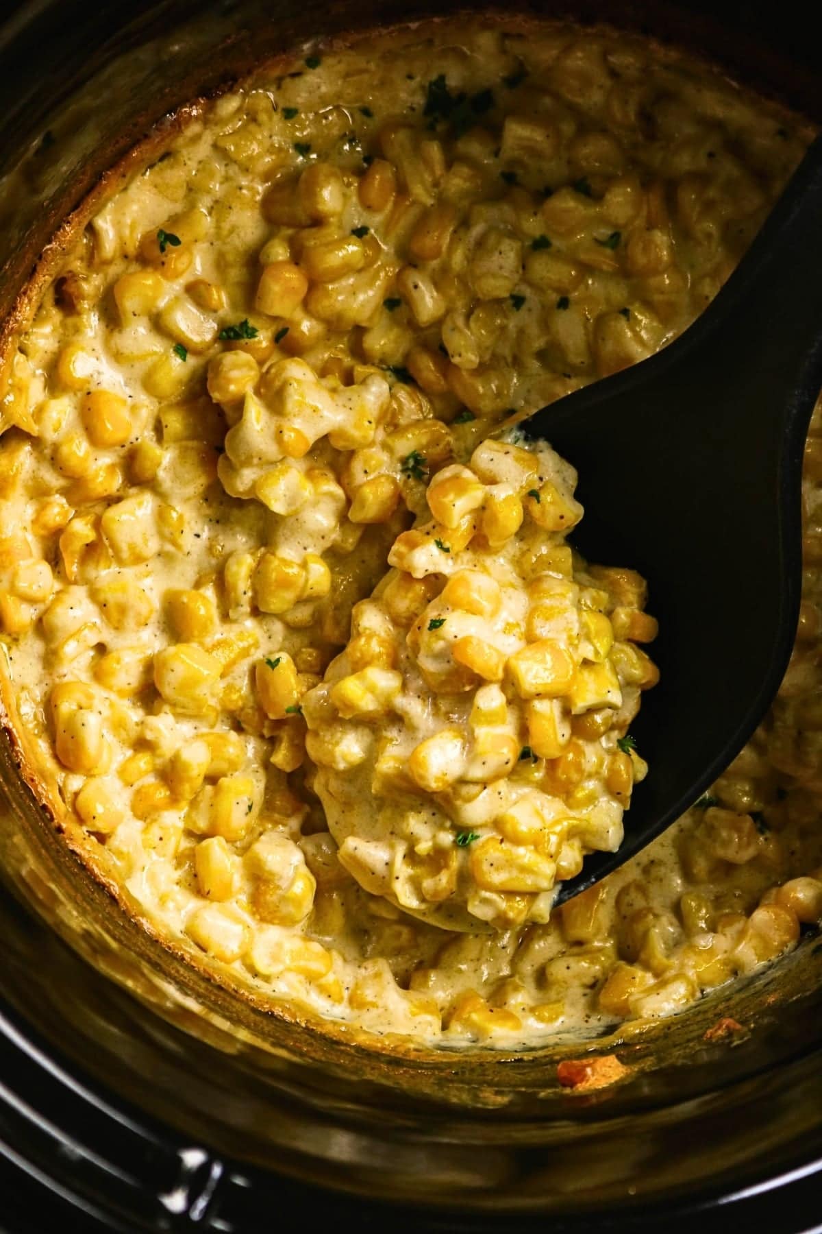 Spoon scooping creamy corn from a pot.