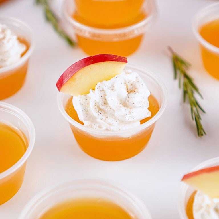 Orange gelatin cup with whipped cream and apple slice garnish.