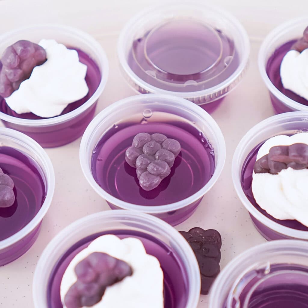 Purple gelatin cups topped with cream and grape-shaped candy.