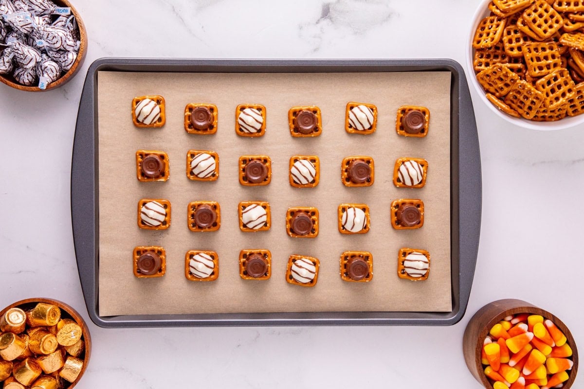 A baking tray with pretzel bites, surrounded by bowls of candy and pretzels.