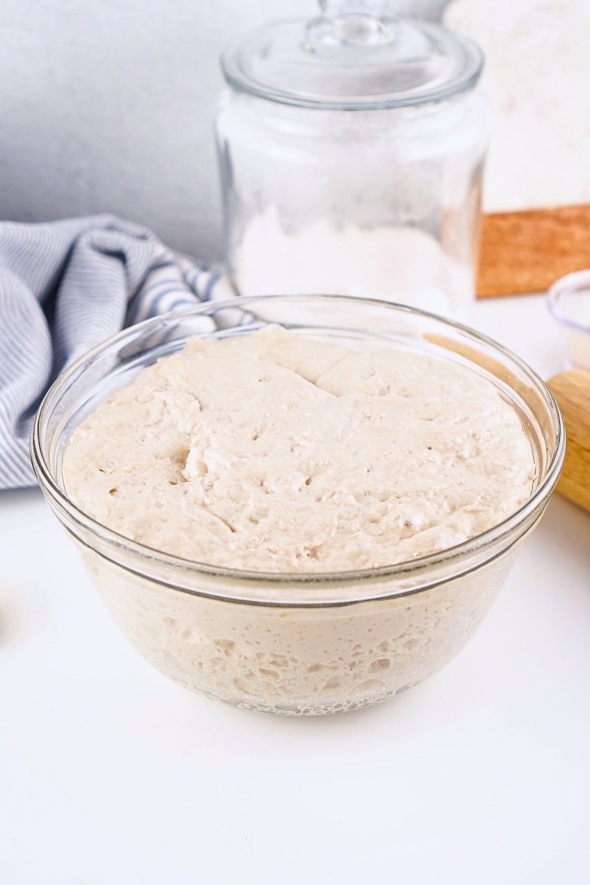 A glass bowl of risen bread dough sits on a white surface.