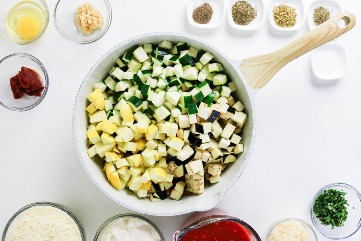Chopped vegetables in a pan surrounded by seasonings and ingredients on a table.