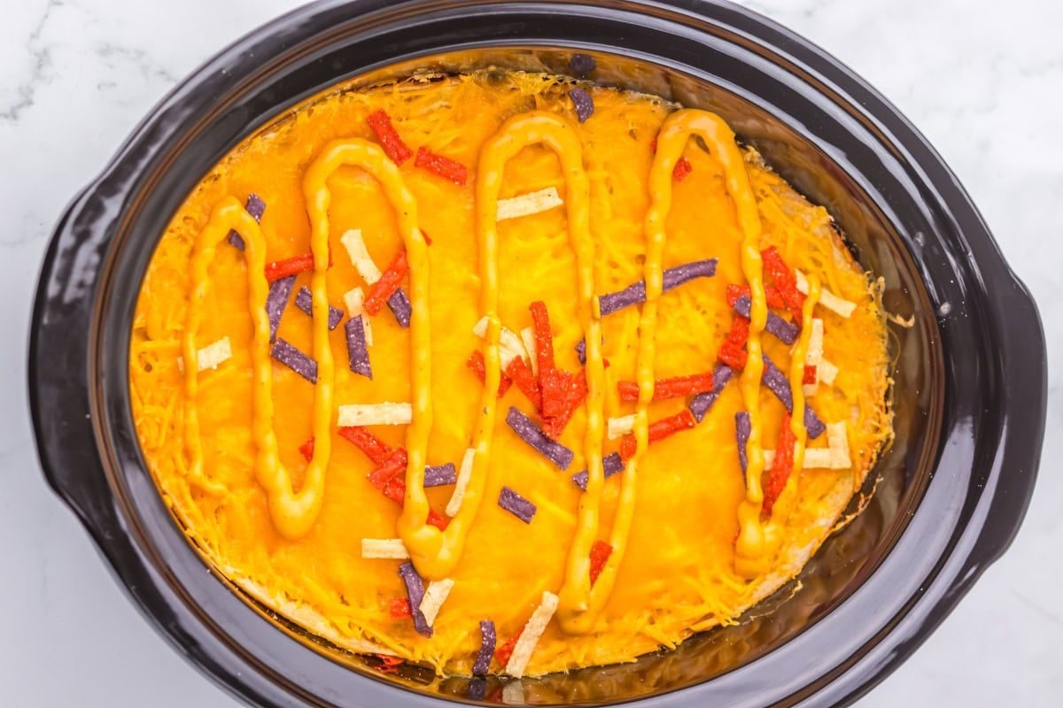 Cheesy casserole in a black slow cooker, topped with sauce and tortilla strips.