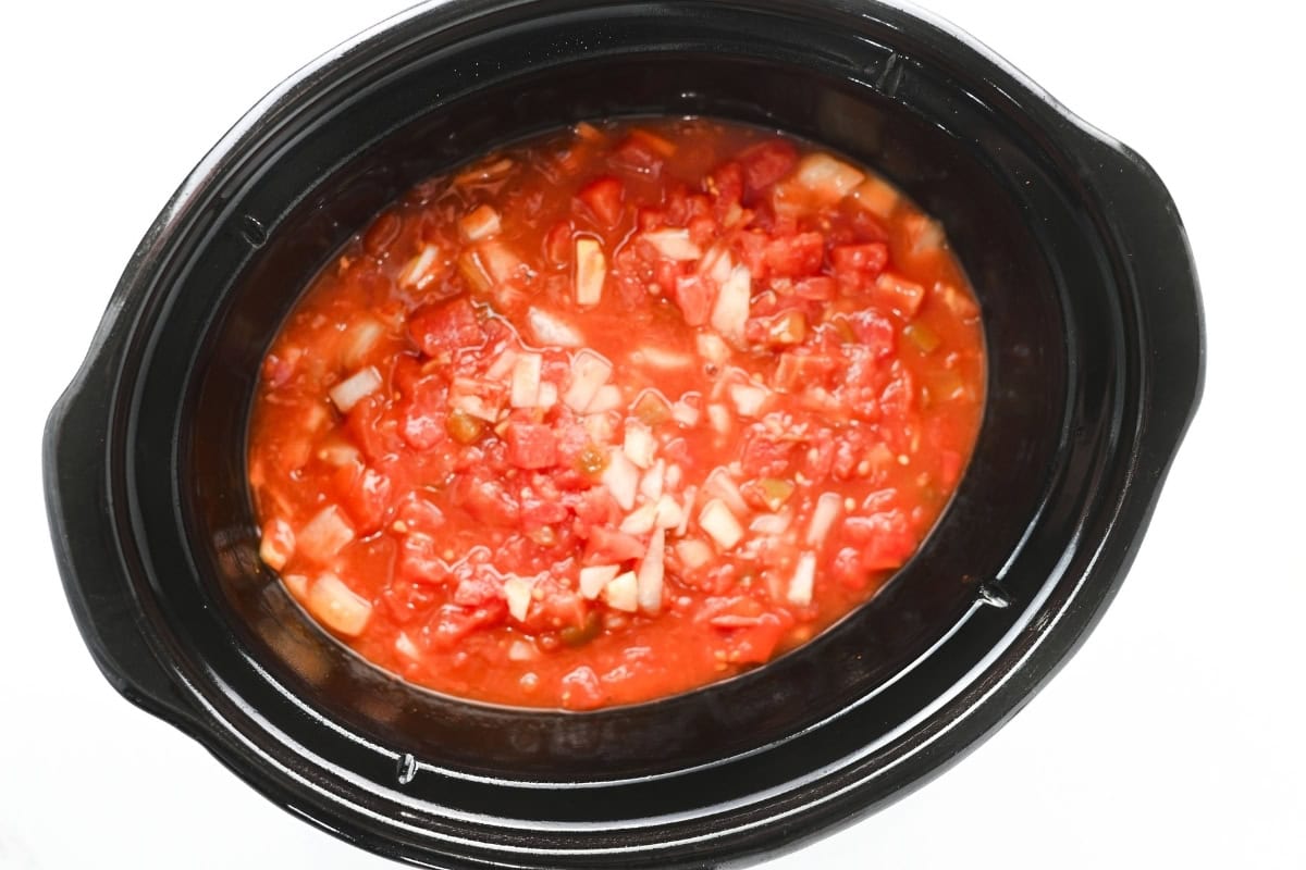 Diced tomatoes and onions in a black slow cooker, ready to cook.