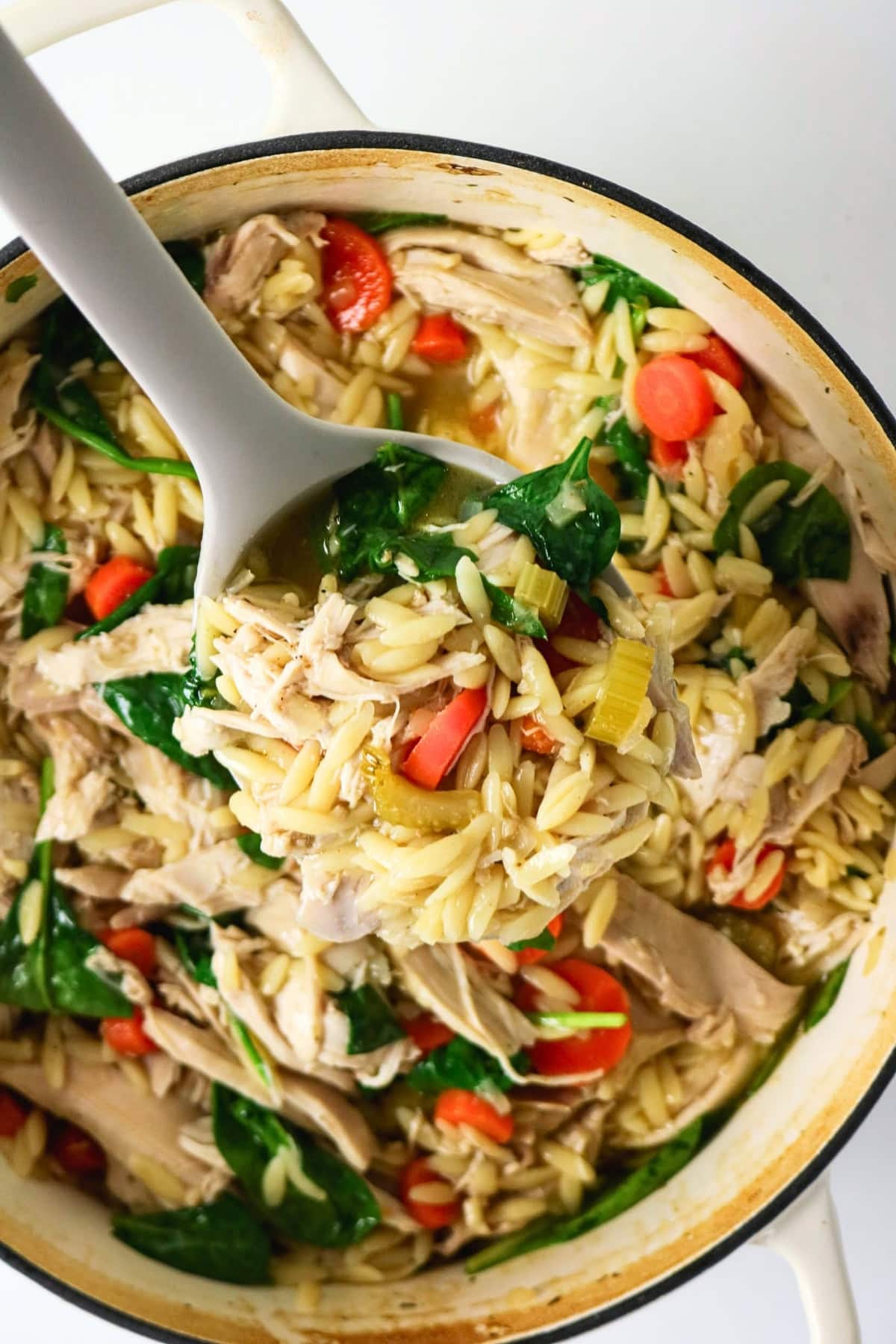 A spoonful of orzo soup with chicken, carrots, and spinach above a pot.