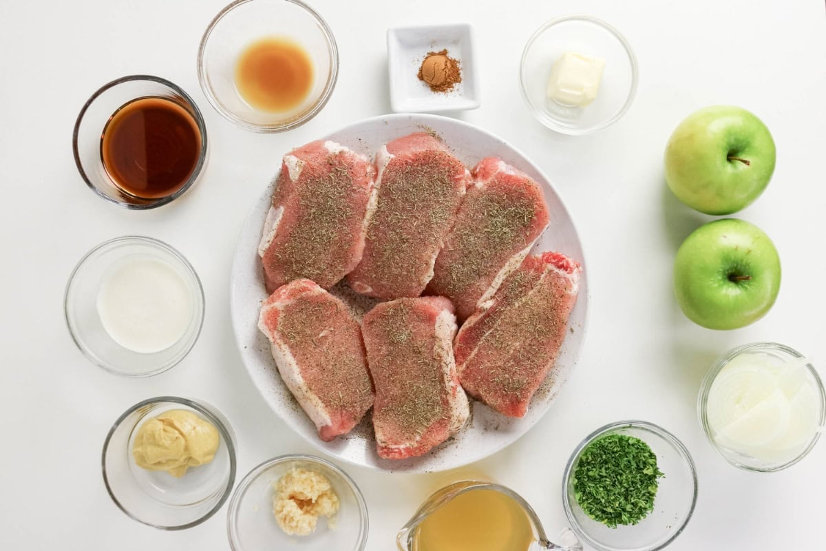 Raw pork chops on a plate, surrounded by various small bowls of ingredients.