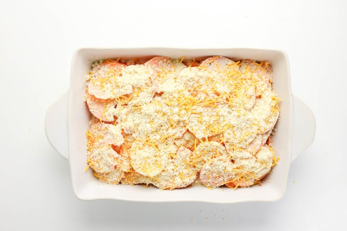 Unbaked casserole topped with grated cheese and breadcrumbs in a white dish.