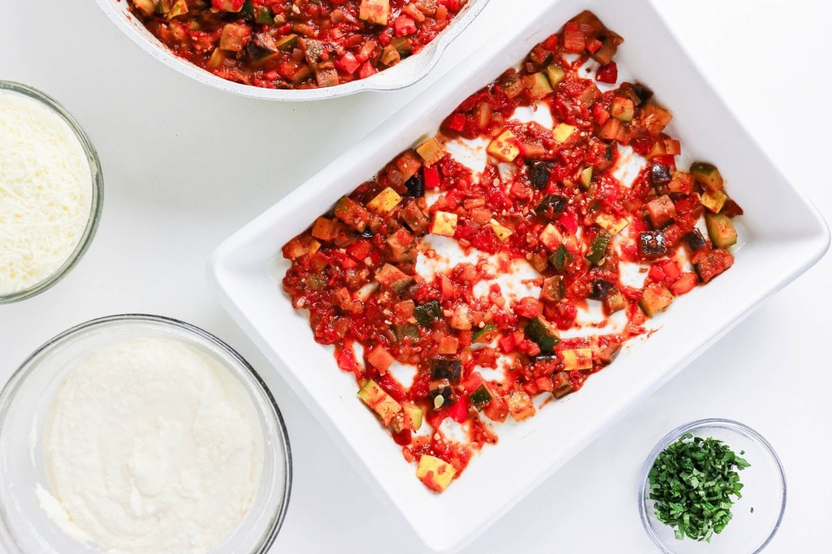 White dish with tomato veggie mix, ricotta, cheese, and herbs on the side.
