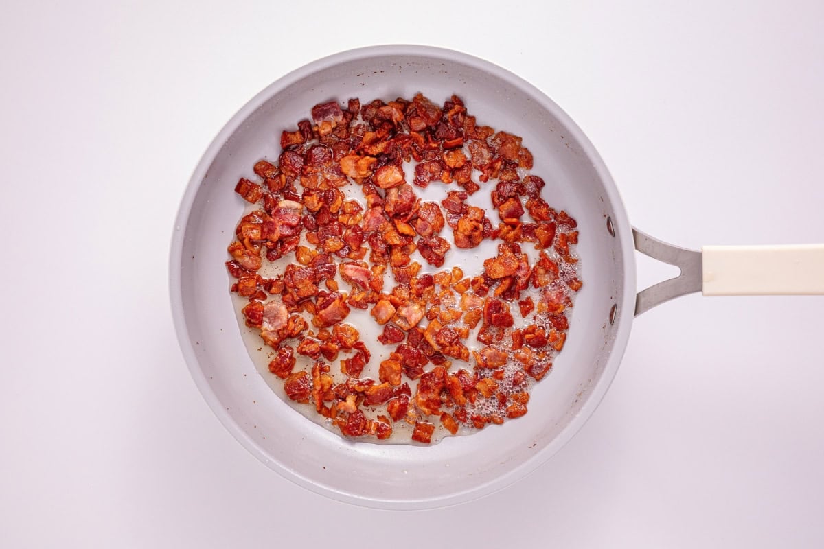 Cooked bacon bits in a white frying pan on a white background.