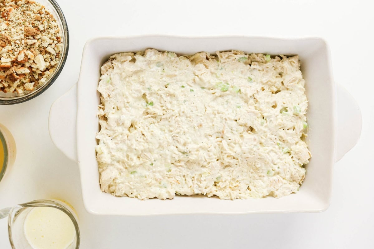 White casserole dish filled with creamy chicken mixture, ready to bake.