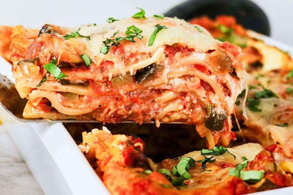 A slice of cheesy vegetable lasagna topped with fresh chopped herbs.