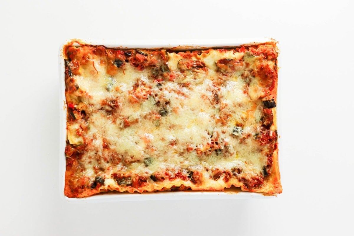 Baked cheesy lasagna in a white dish on a white background.