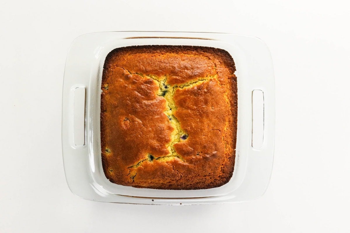 Golden baked cake in a square glass dish on a white background.