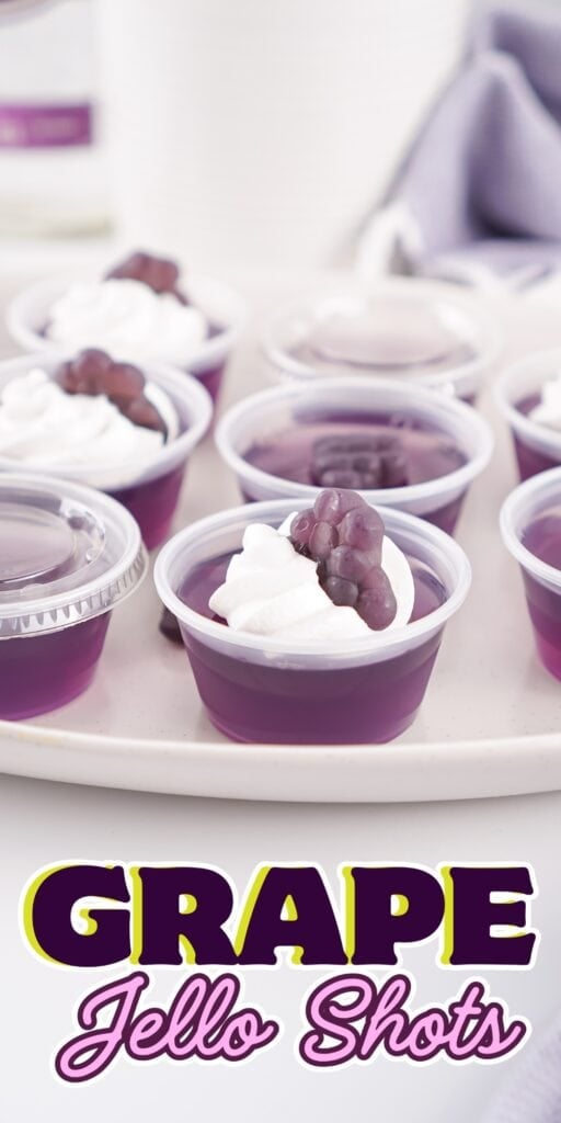 Purple jello shots with whipped cream and grape topping on a white tray.