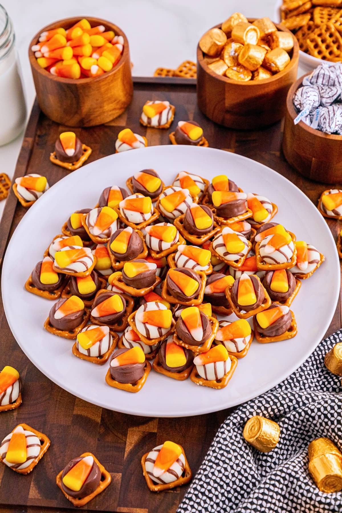Plate of pretzel treats topped with candy corn and chocolates on a wooden table.